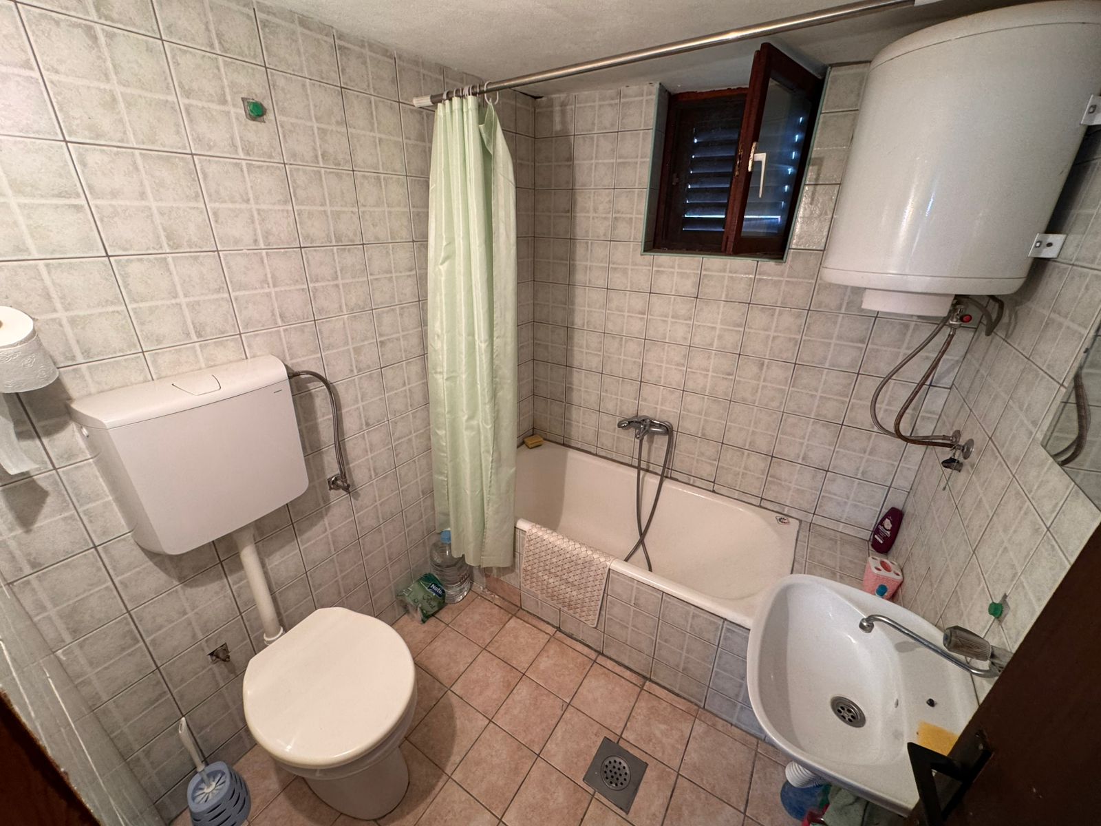 Modern tiled bathroom in Ulcinj property: toilet, eco water heater, tub with shower, sink, window&mdash;exclusive at montenegro-listings.me.