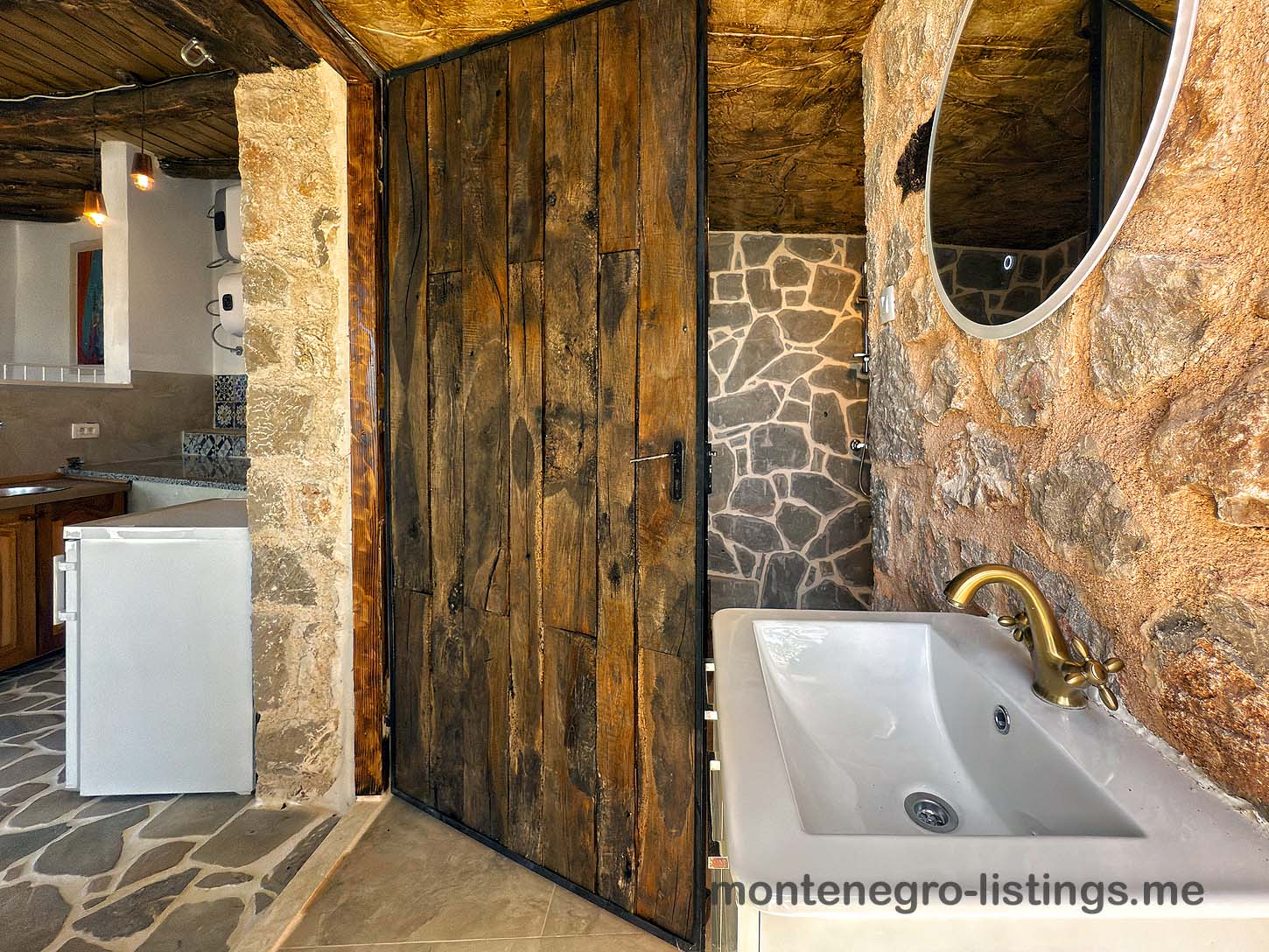 Elegant rustic bathroom with stone walls, wood door, chic brass accents; ideal Ulcinj investment via montenegro-listings.me by ekosphere doo.