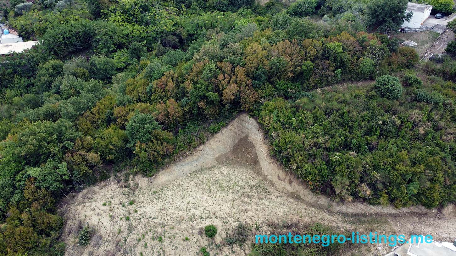 Prime triangular plot in Ulcinj, bordered by lush greenery and partial rooftops. Invest via montenegro-listings.me, a project of ekosphere doo.