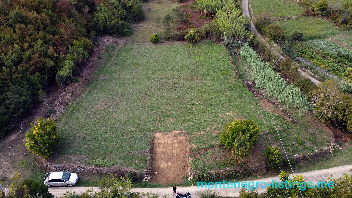 Prime rectangular plot for sale in Ulcinj, Montenegro—lush green land bordered by trees, road access, ideal for investors.
