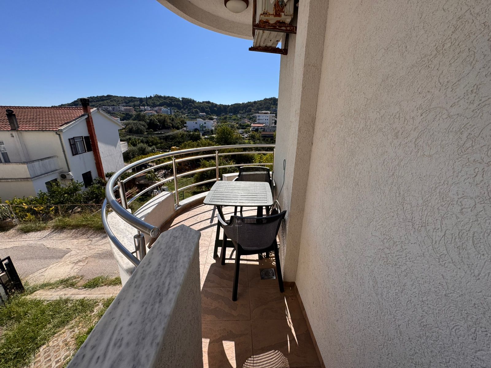 Charming Ulcinj balcony with glass-top table, seating for two, scenic hills, and tranquil views&mdash;exclusive on montenegro-listings.me by ekosphere doo.