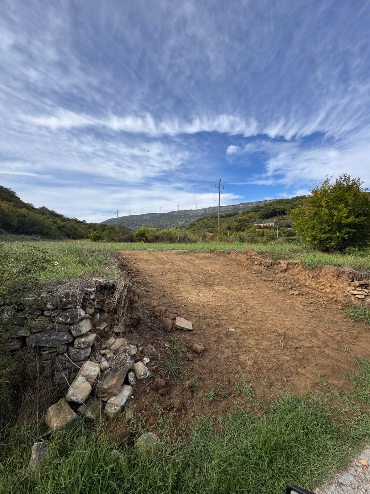 Scenic Ulcinj land for sale: serene grassy terrain, green hills, wind turbines, and investment potential from ekosphere doo.