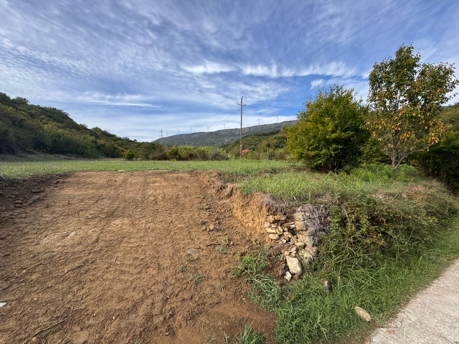 Prime Ulcinj land for sale: cleared plot with lush grassy area, trees, hill views, and infrastructure&mdash;exclusive on montenegro-listings.me.