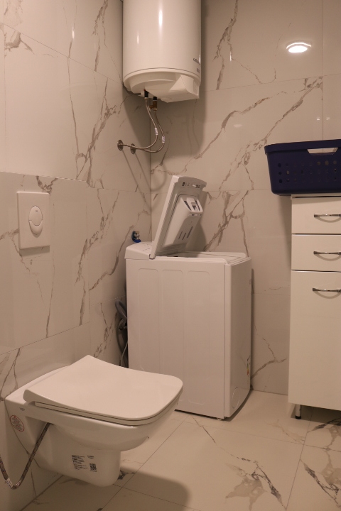Modern Ulcinj bathroom with marble tiles, wall-mounted toilet, washer, water heater—investment opportunity at montenegro-listings.me by ekosphere doo.