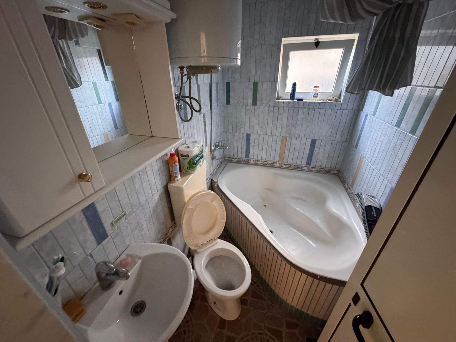 Modern Ulcinj bathroom with corner bathtub, blue-white tiles, window, quality fittings&mdash;an ideal real estate investment. Montenegro-listings.me by ekosphere doo.