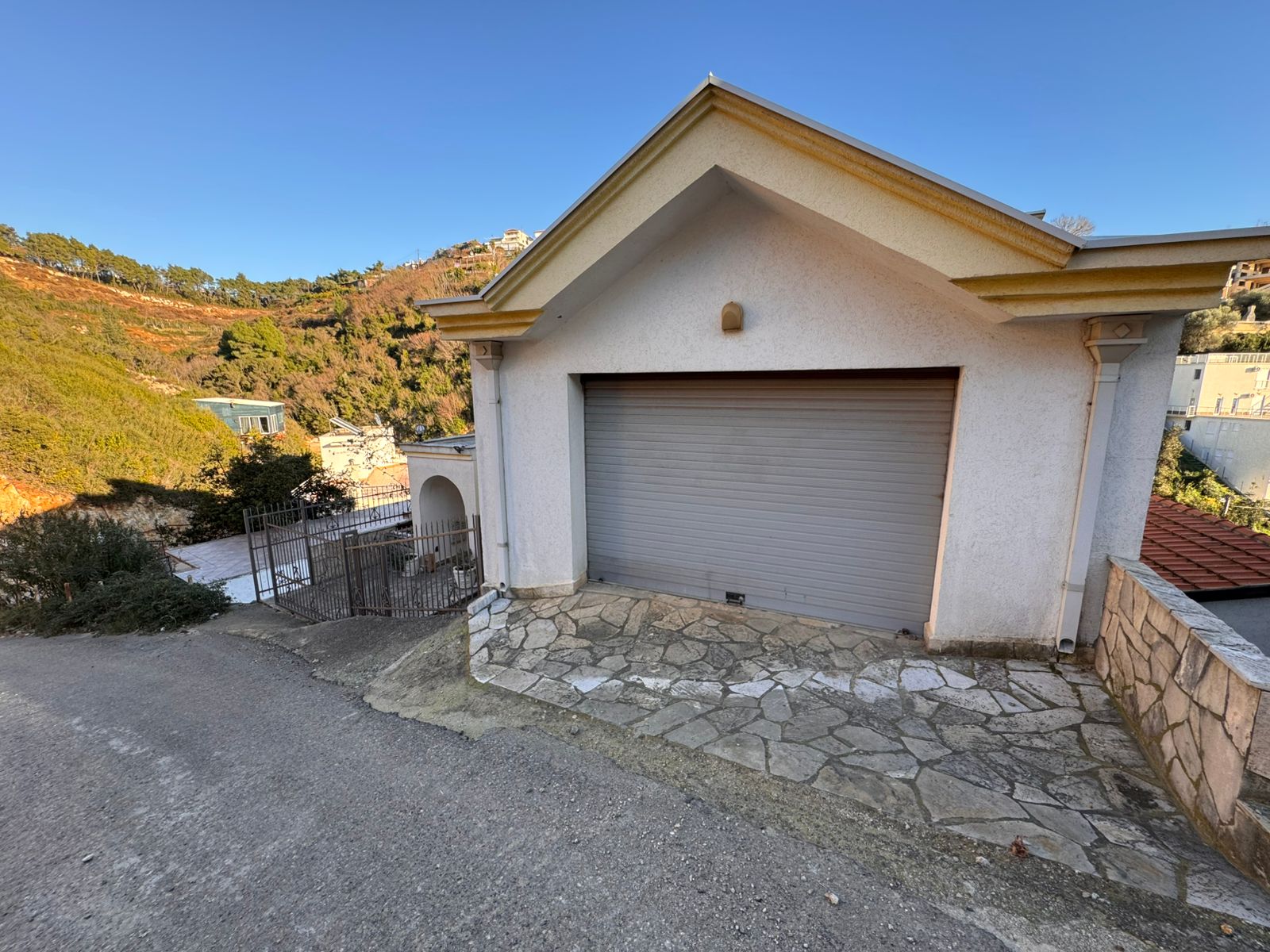 Modern white garage with secure gray door on a sloped lot, stone-paved drive, scenic Ulcinj views&mdash;exclusive at montenegro-listings.me.