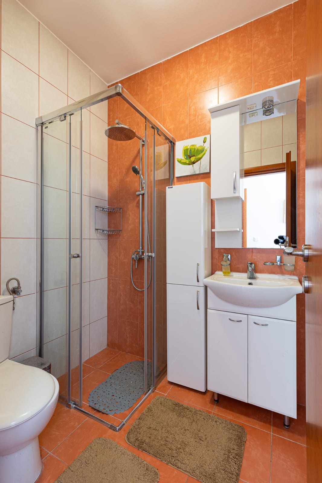 Modern Ulcinj bathroom with stylish orange-white tiles, glass shower, premium fixtures. Exclusive on montenegro-listings.me by ekosphere doo.