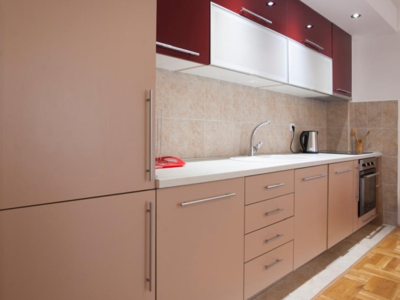 Stylish modern kitchen in Ulcinj, Montenegro: beige and maroon cabinets, parquet floors, tiled backsplash. Listed on montenegro-listings.me by ekosphere doo—ideal property investment.