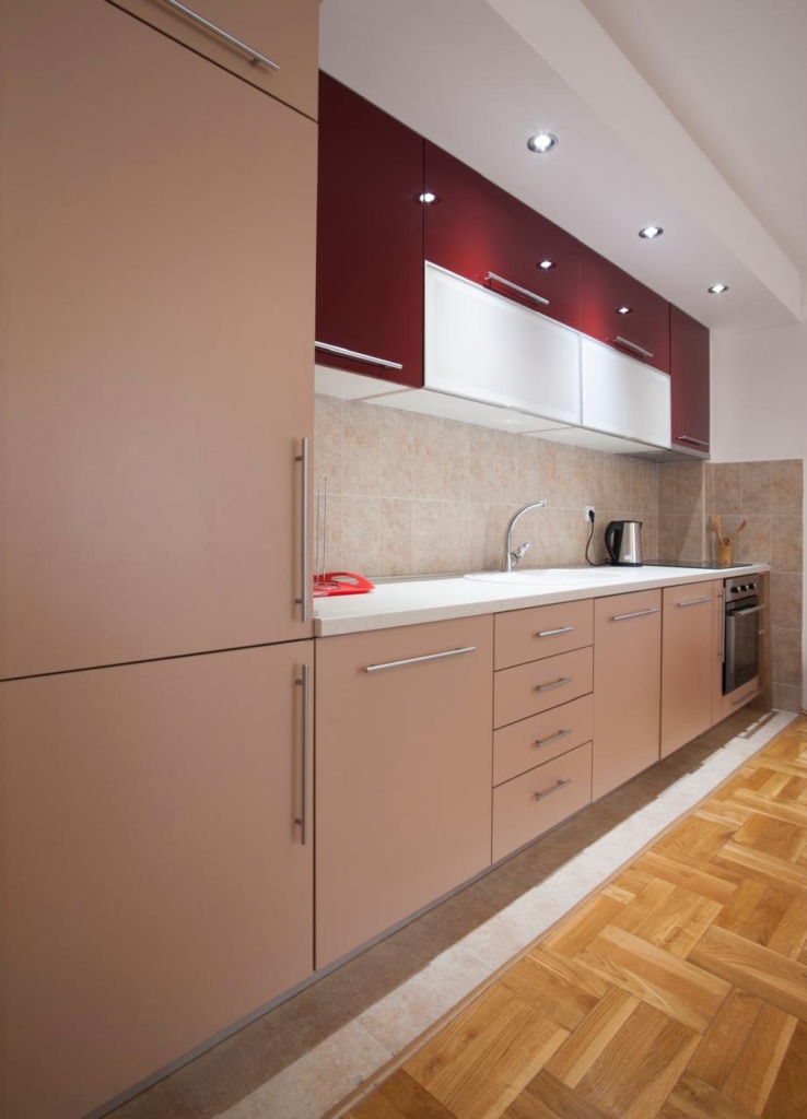 Stylish modern kitchen in Ulcinj, Montenegro: beige and maroon cabinets, parquet floors, tiled backsplash. Listed on montenegro-listings.me by ekosphere doo—ideal property investment.