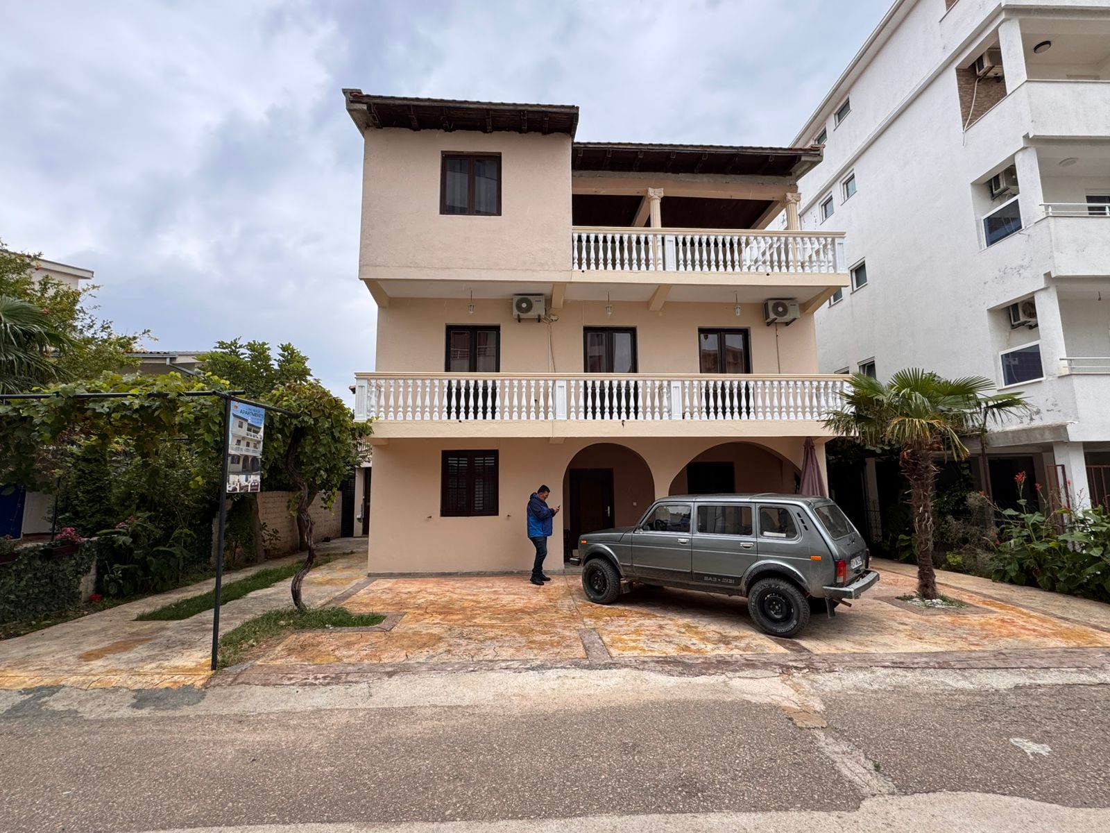 Modern three-story beige residence with balconies, tiled roof, and palm—prime Ulcinj investment via montenegro-listings.me by ekosphere doo.