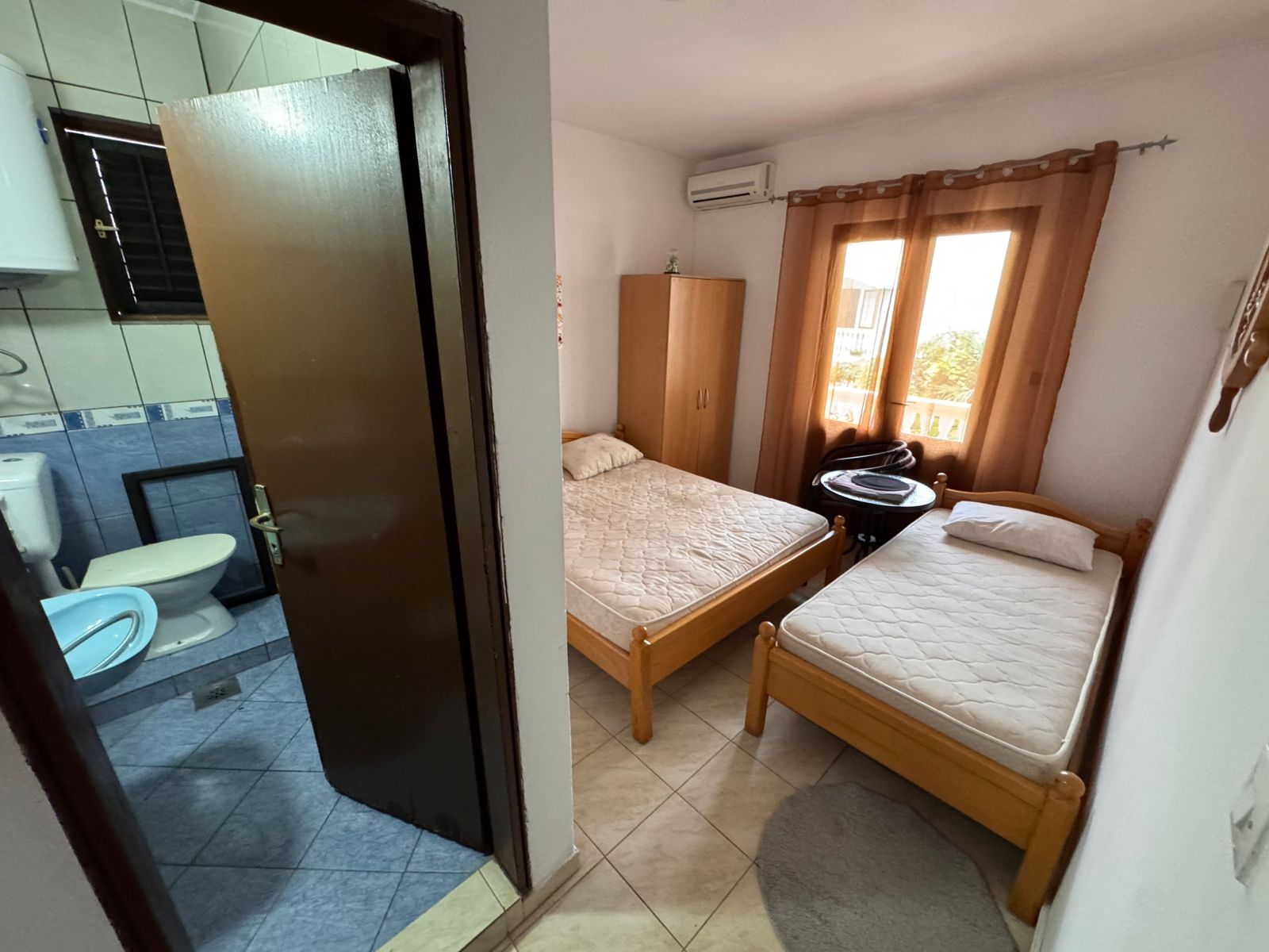 Bright Ulcinj bedroom with twin beds, wardrobe, window, and modern tiled bathroom—an ideal investment via montenegro-listings.me.