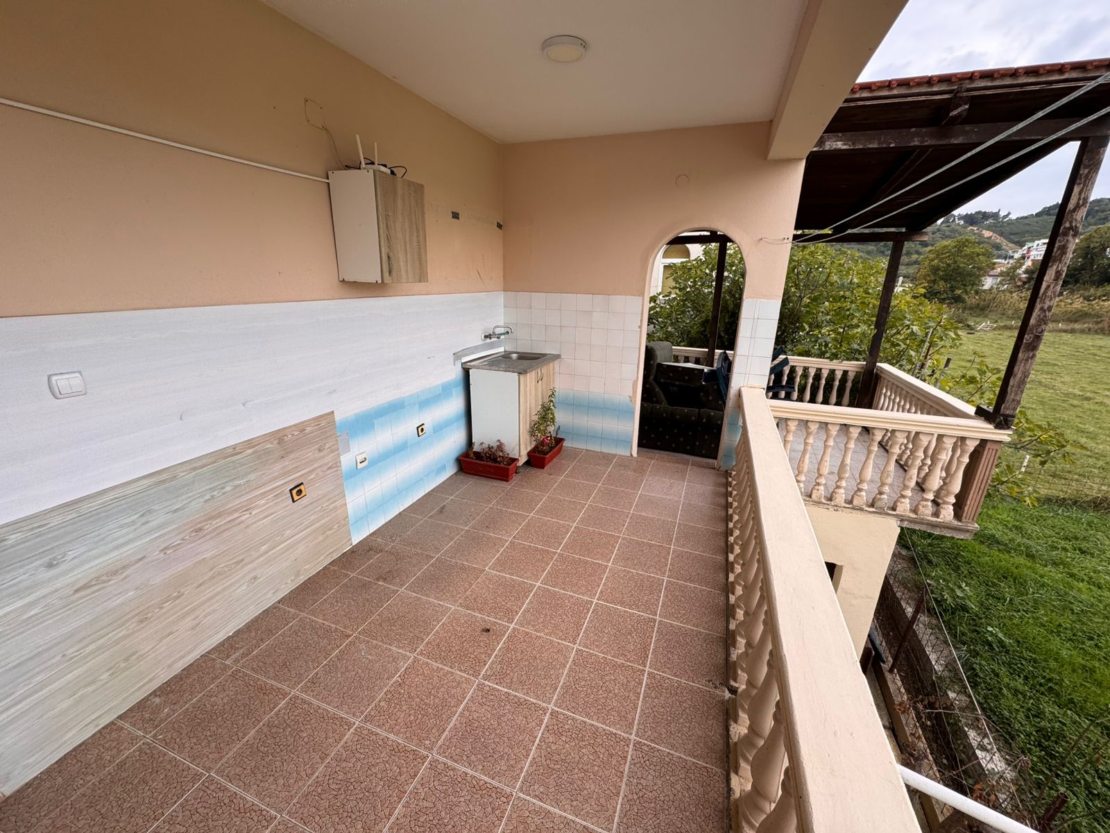 Spacious tiled balcony in Ulcinj with sink, covered seating, and peaceful green views—ideal Montenegro investment at montenegro-listings.me.