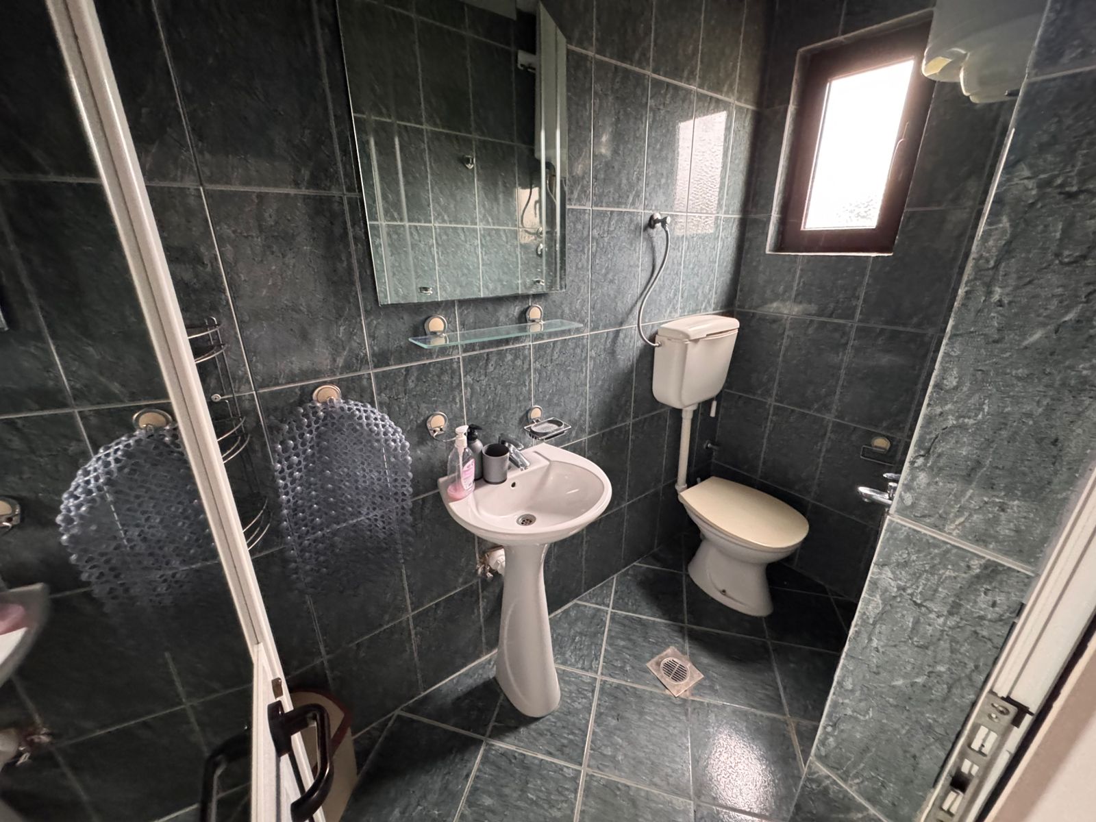 Stylish bathroom with elegant dark green tiles, modern fixtures, natural light—prime Ulcinj investment via montenegro-listings.me by ekosphere doo.
