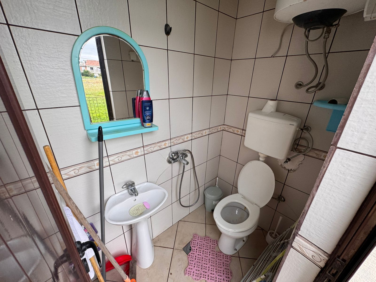 Modern tiled bathroom featuring a sink, mirror, and toilet, water heater, pink mat; ideal Ulcinj investment via montenegro-listings.me.