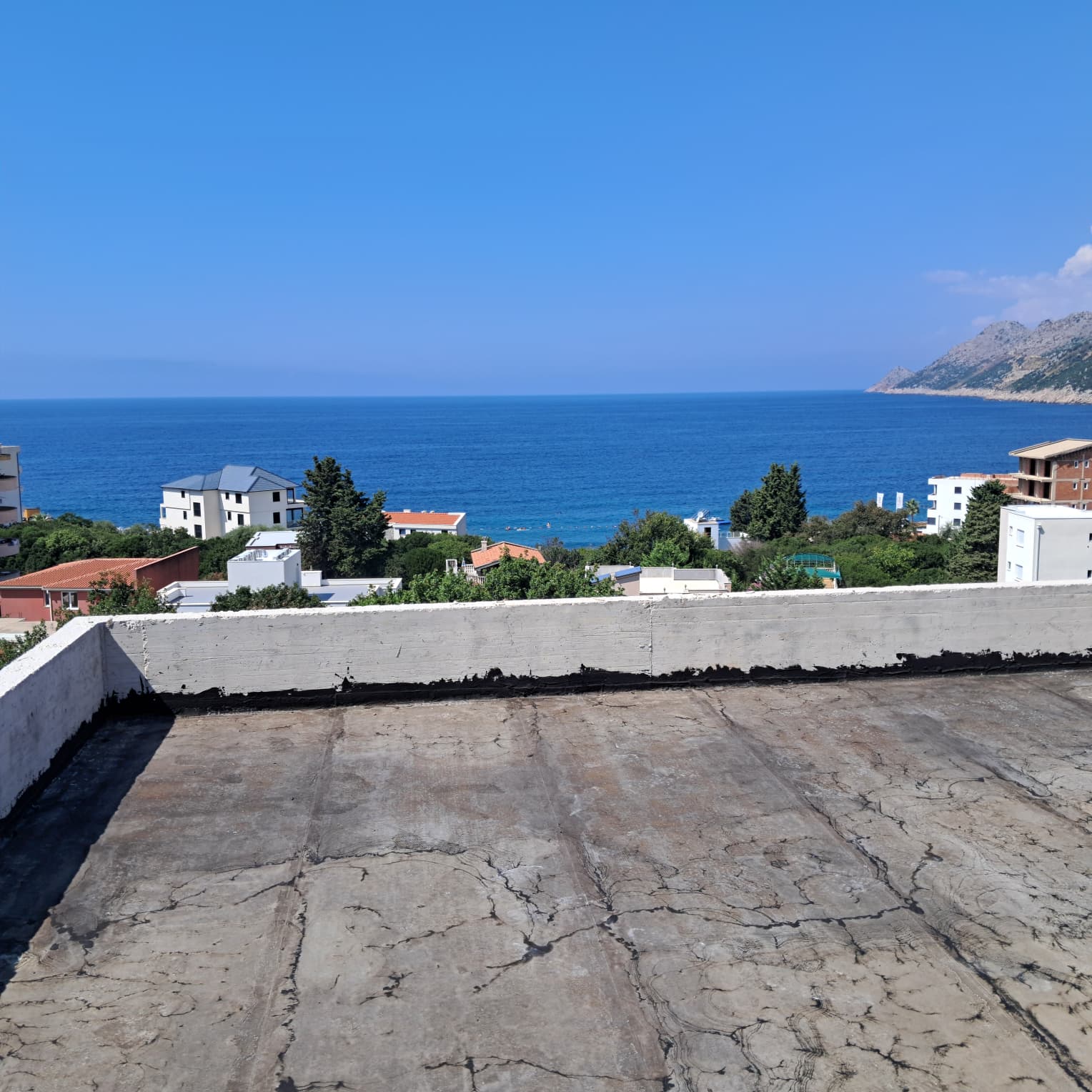 Panoramic rooftop view over Ulcinj: residential homes, lush greenery, Adriatic Sea—prime Montenegro real estate by ekosphere doo.