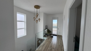 Elegant hallway in Ulcinj home with wood floors, modern chandelier, glass railing—exclusive property via montenegro-listings.me by ekosphere doo.