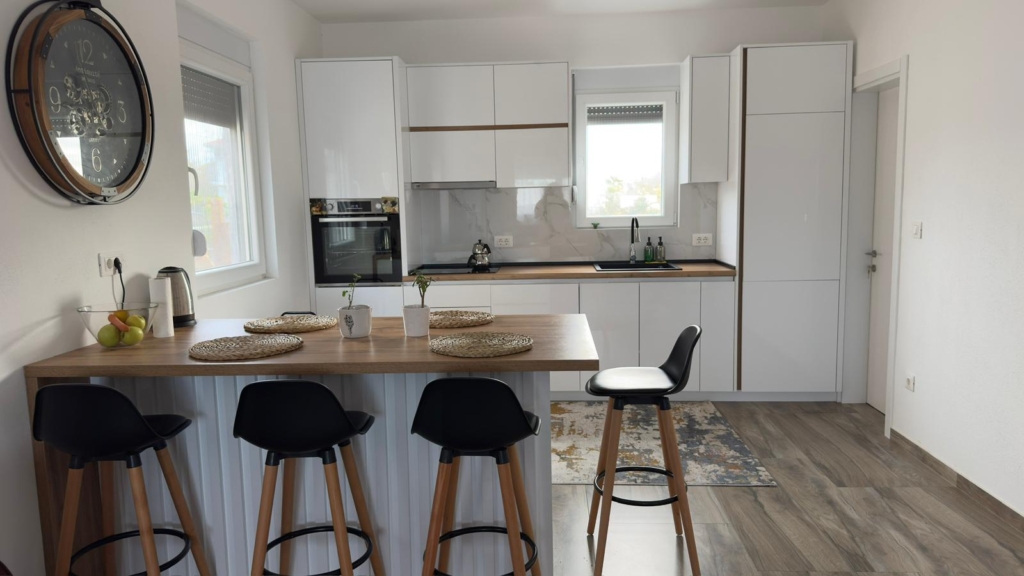Sleek white kitchen in Ulcinj with wood counters, bar stools, built-in oven—ideal Montenegro property on montenegro-listings.me by ekosphere doo.