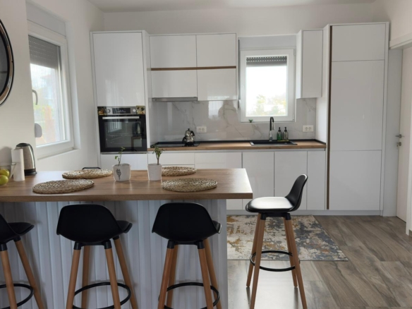 Sleek white kitchen in Ulcinj with wood counters, bar stools, built-in oven—ideal Montenegro property on montenegro-listings.me by ekosphere doo.