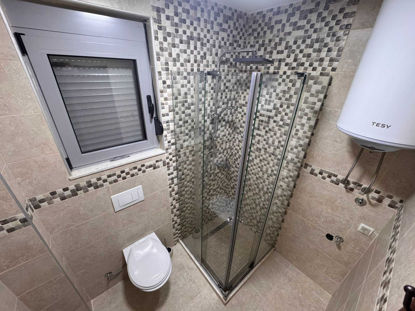 Modern Ulcinj bathroom: beige tiles, glass corner shower, wall toilet, frosted window&mdash;investment property at montenegro-listings.me by ekosphere doo.