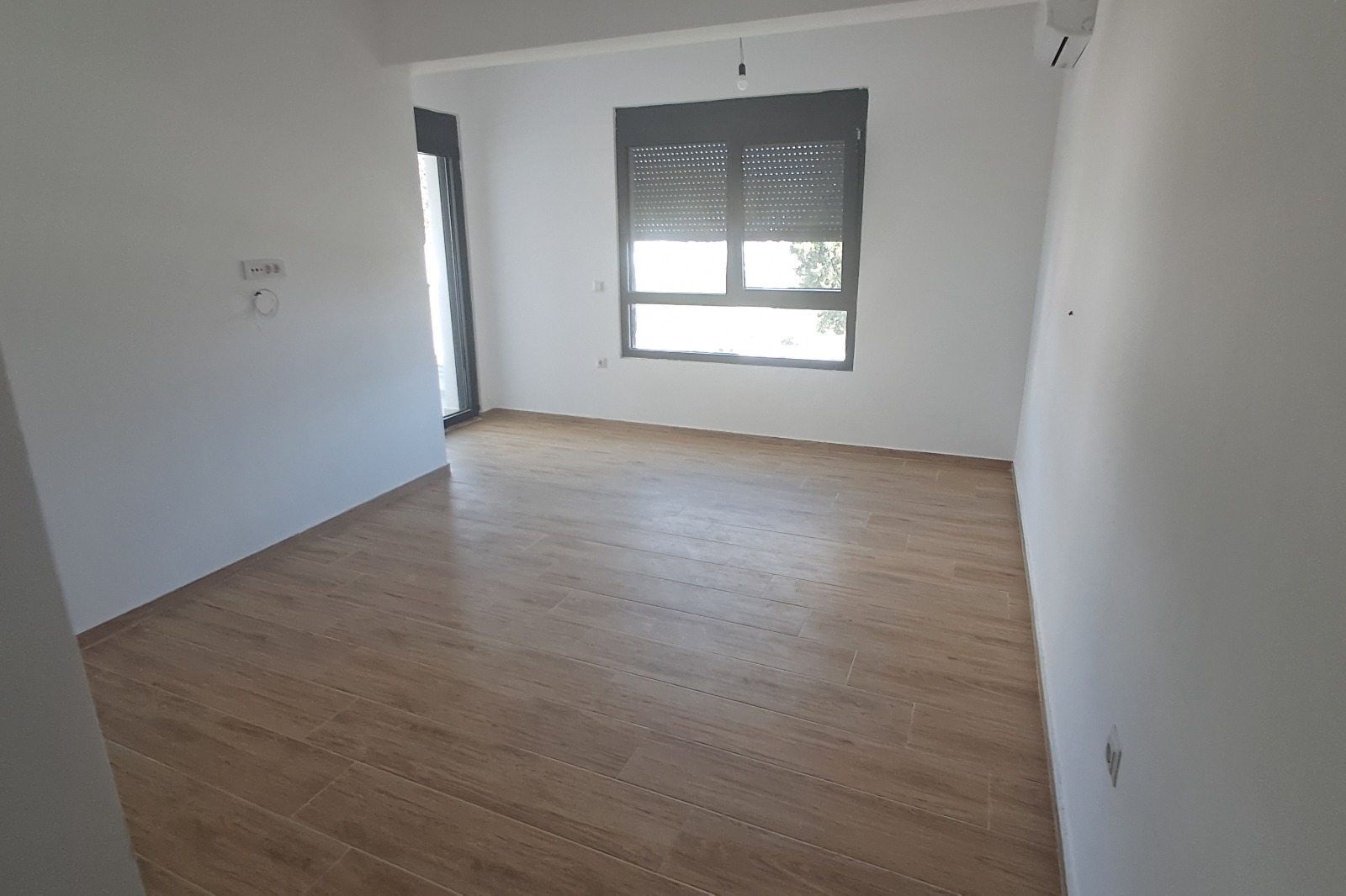 Modern, bright room in Ulcinj with wood-look tile floors, AC, balcony access—ideal Montenegro investment via montenegro-listings.me by ekosphere doo.