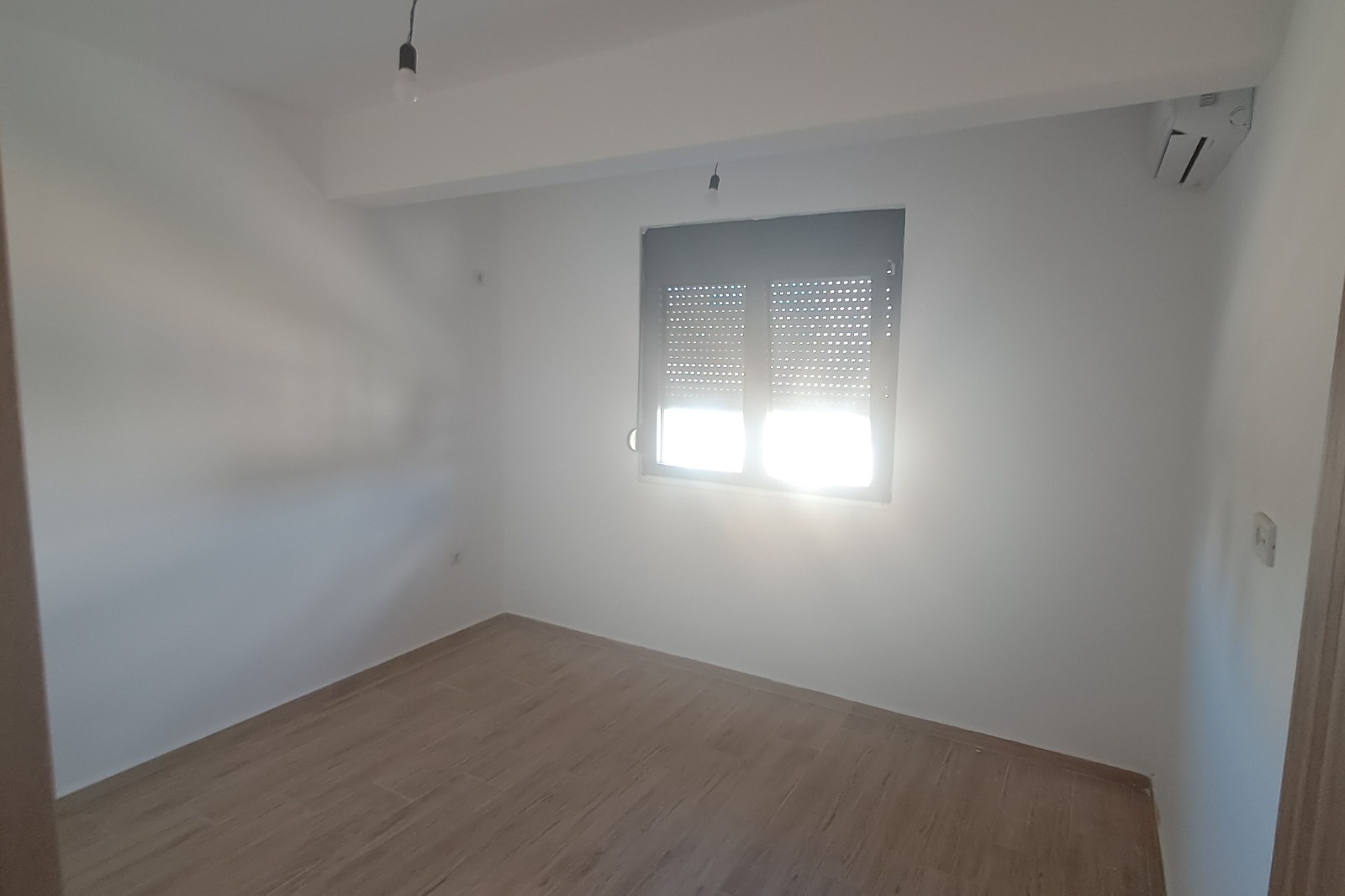 Bright, modern Ulcinj apartment with white walls, wood flooring, AC unit; sunlight through window. Invest via montenegro-listings.me by ekosphere doo.