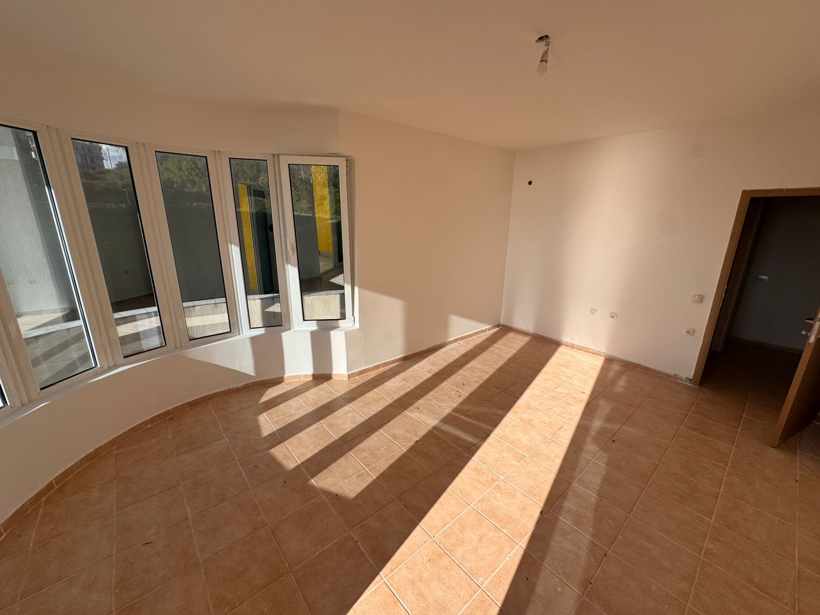 Bright, unfurnished Ulcinj property with tiled floors, curved panoramic windows, and cream walls. Featured on montenegro-listings.me.