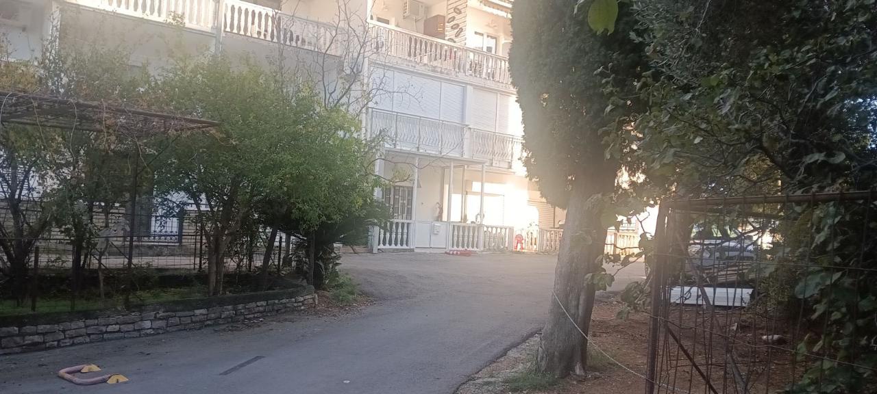 Charming Ulcinj property: white multi-story building with balconies, lush greenery, sunlit paved road&mdash;exclusive on montenegro-listings.me by ekosphere doo.