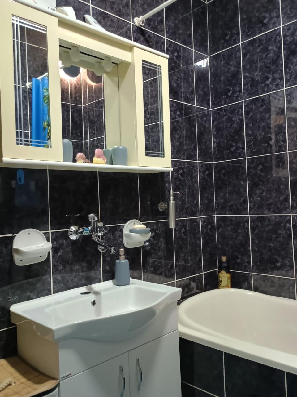 Modern bathroom in Ulcinj with stylish dark tiles, contemporary sink, lit mirror, and tub&mdash;ideal Montenegro real estate investment.