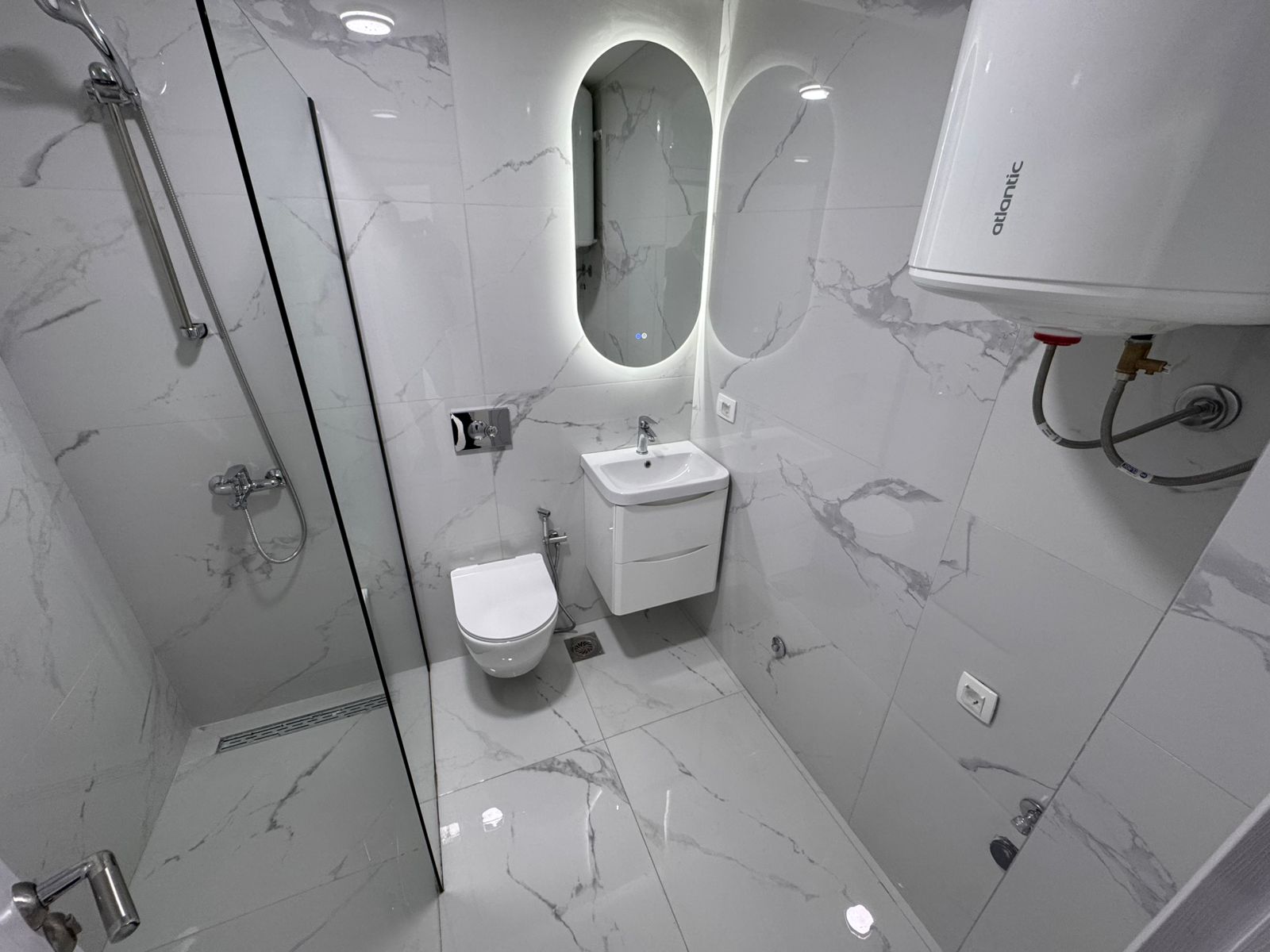 Ulcinj luxury bathroom: marble-look tiles, wall-mounted toilet, sleek sink, glass shower&mdash;prime property at montenegro-listings.me.