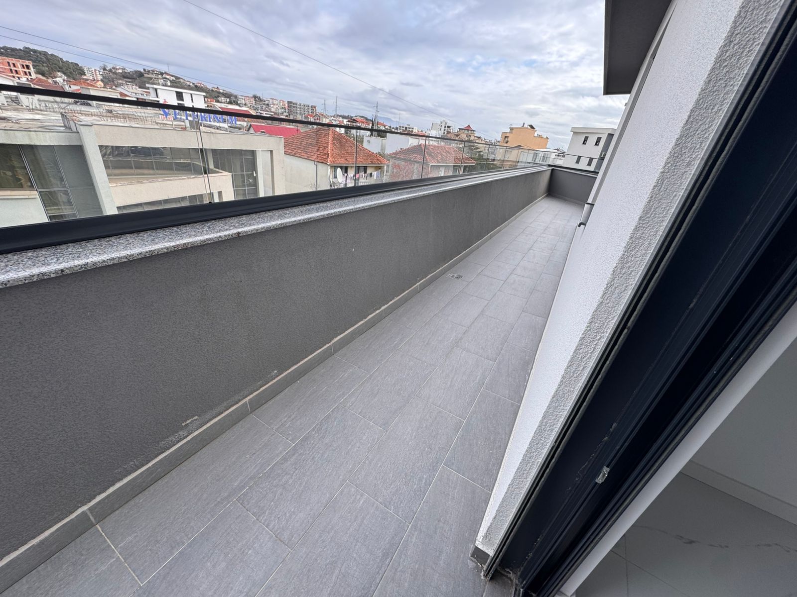 Modern balcony with stylish gray tiles and glass railing, offering stunning Ulcinj rooftop views&mdash;exclusive at montenegro-listings.me, a project of ekosphere doo.