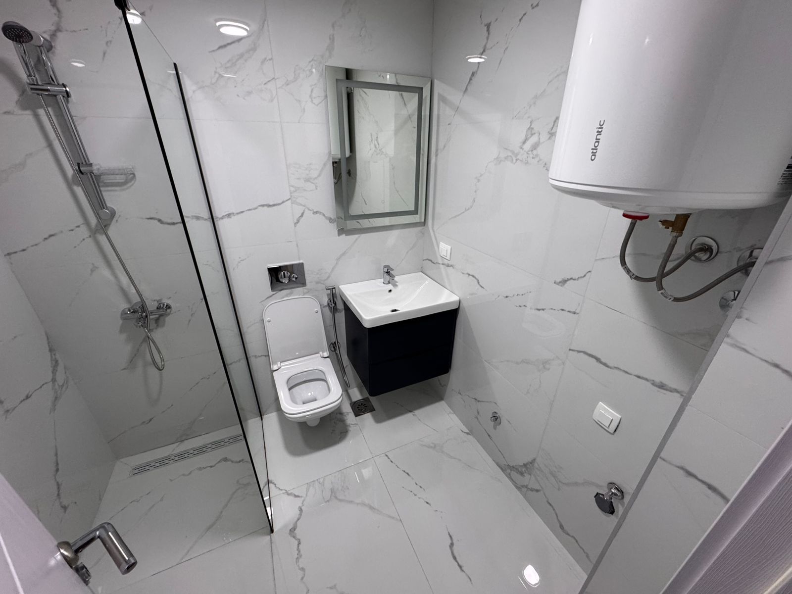 Luxury bathroom in Ulcinj with marble-style tiles, glass shower, wall-hung toilet&mdash;exclusive listing by ekosphere doo at montenegro-listings.me.