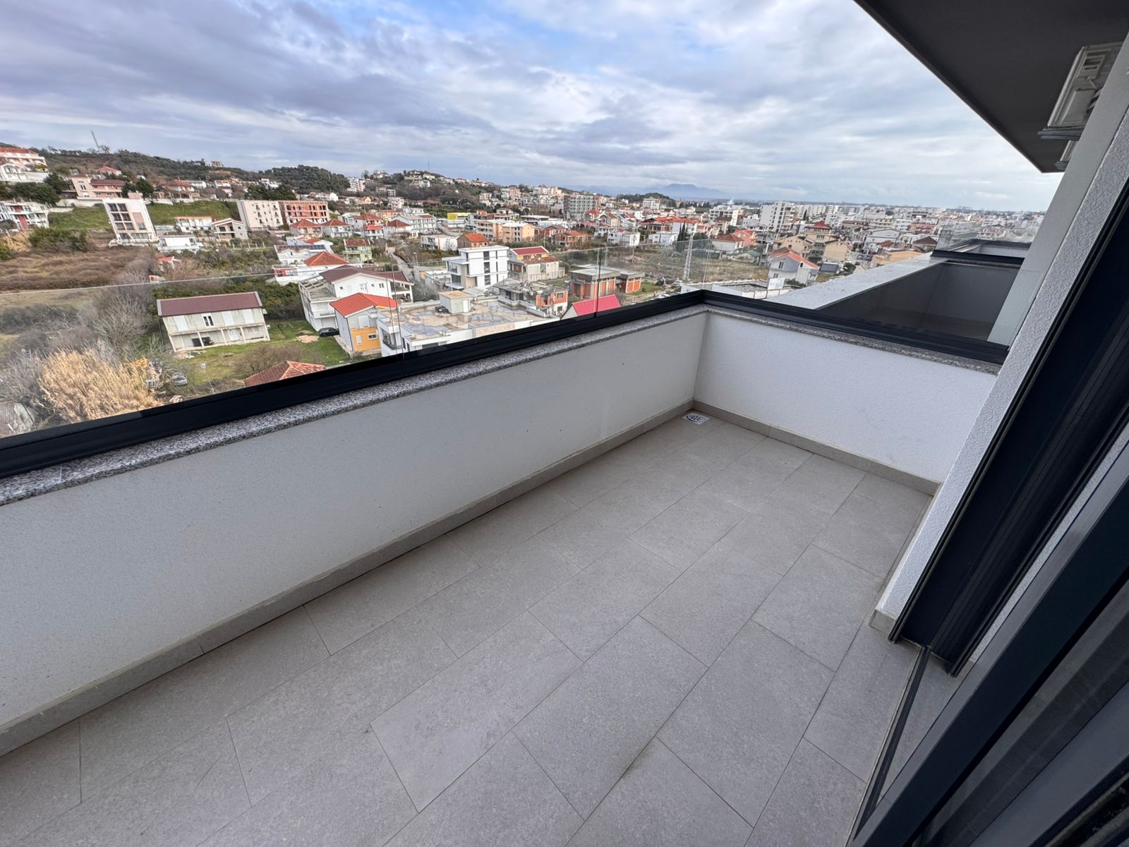 Modern, spacious balcony with sleek glass railing and light gray tiles, boasting stunning Ulcinj views&mdash;exclusive on montenegro-listings.me by ekosphere doo.
