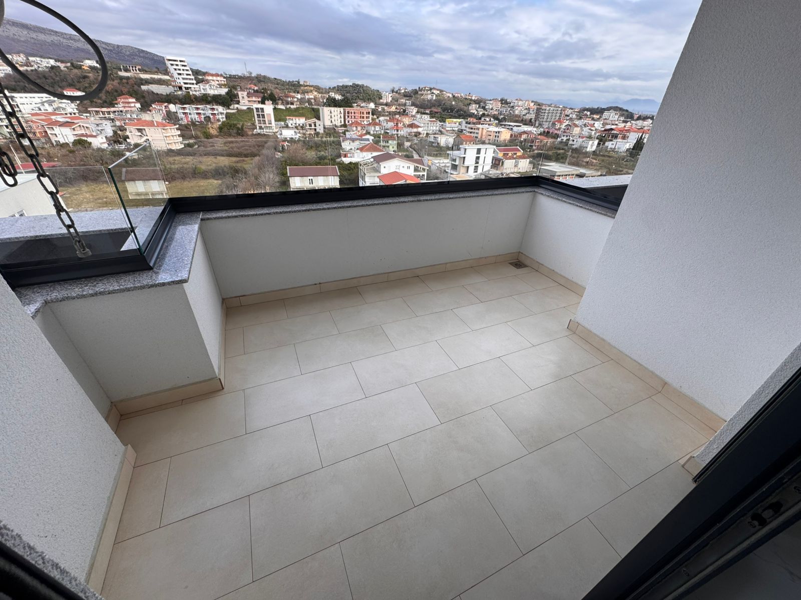 Spacious tiled balcony with white walls and black railing, offering panoramic Ulcinj cityscape views&mdash;prime Montenegro investment. Discover more on montenegro-listings.me by ekosphere doo.