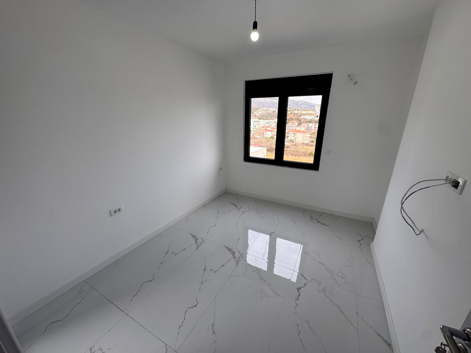 Modern Ulcinj property: bright room with white walls, marble tile floors, large window. Prime investment. Montenegro-listings.me/Ekosphere doo.
