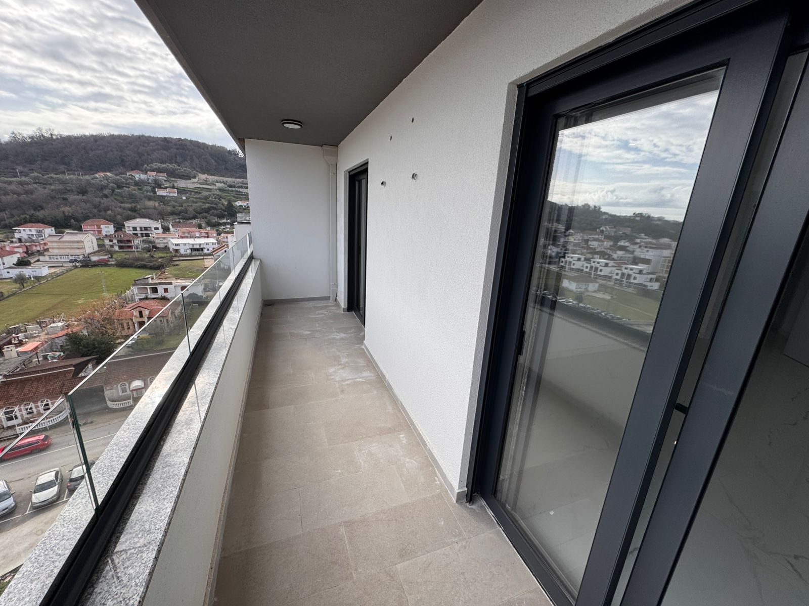 Spacious balcony with modern tiles, glass doors, and stunning views over Ulcinj&rsquo;s homes and hills&mdash;exclusive at montenegro-listings.me.