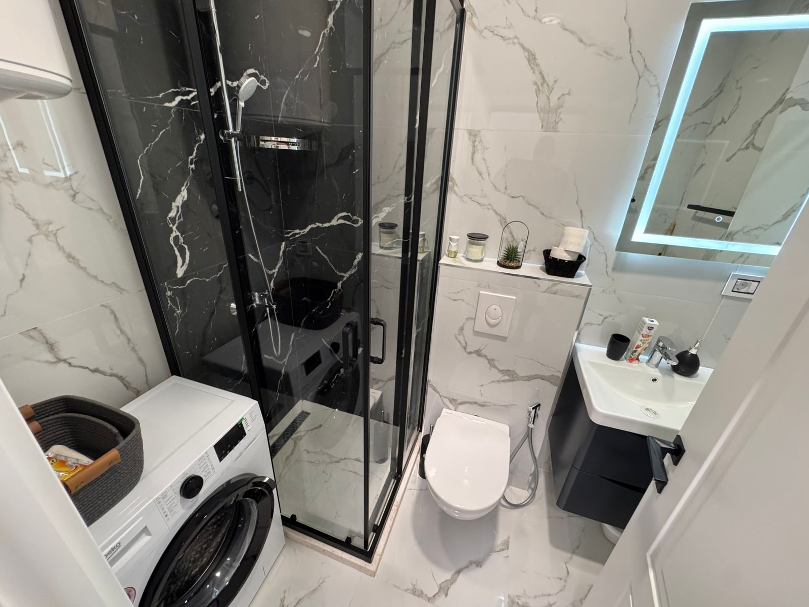 Elegant Ulcinj bathroom: glass shower, wall-mounted toilet, washer, sink with mirror, luxury marble décor. Exclusive at montenegro-listings.me by ekosphere doo.