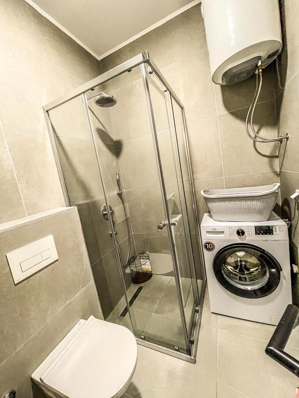 Modern Ulcinj bathroom with beige tiles, glass shower, washing machine, and smart fixtures&mdash;investment via montenegro-listings.me by ekosphere doo.