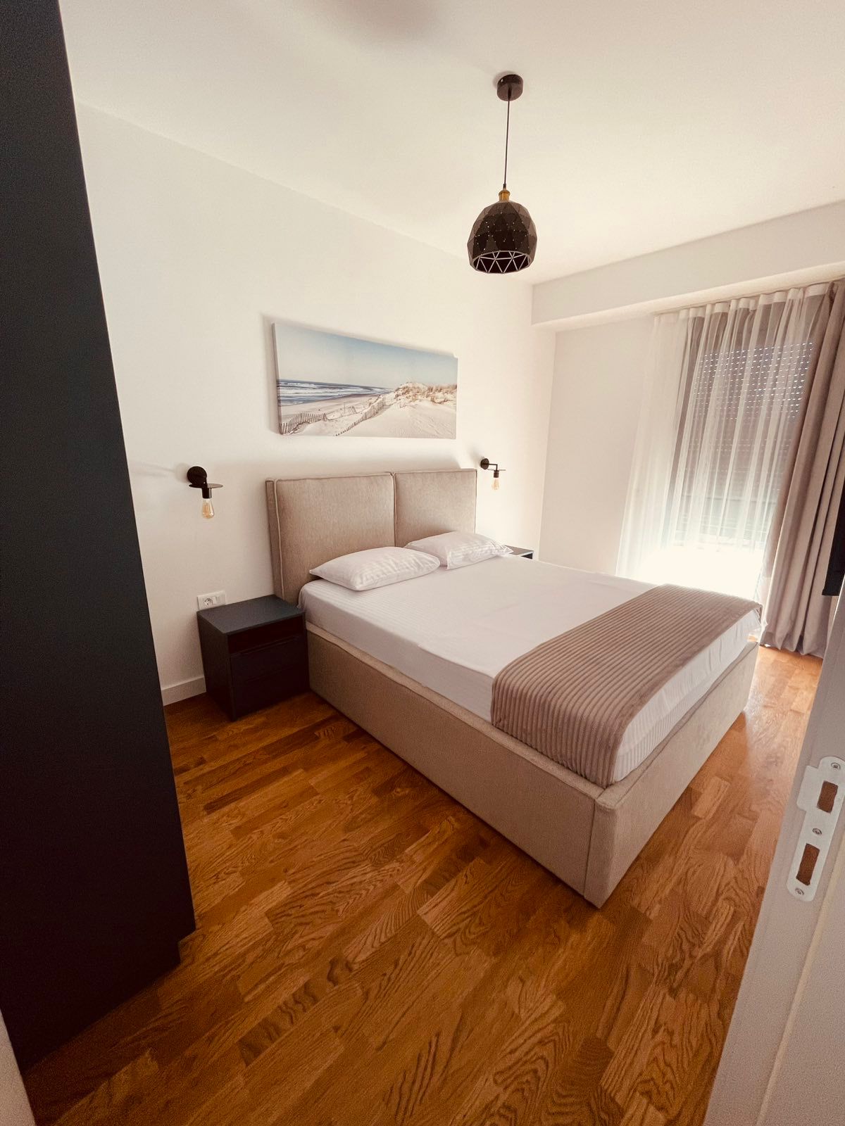 Elegant modern bedroom in Ulcinj, Montenegro with stylish bed, wood floors, and natural light. Exclusive at montenegro-listings.me by ekosphere doo.