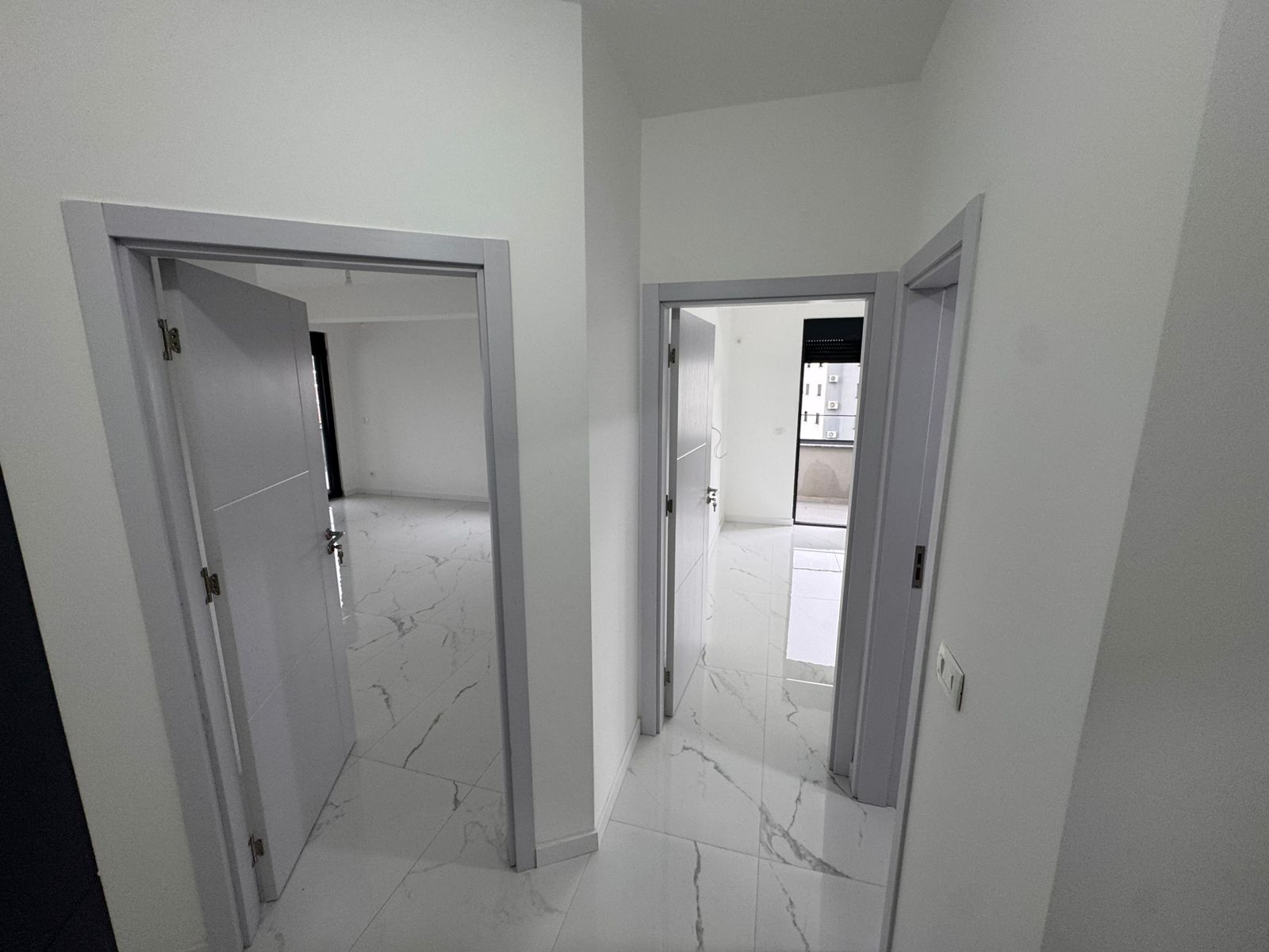 Bright hallway in Ulcinj property with modern white walls, luxury veined tile floors, and sunlit rooms&mdash;exclusive at montenegro-listings.me by ekosphere doo.