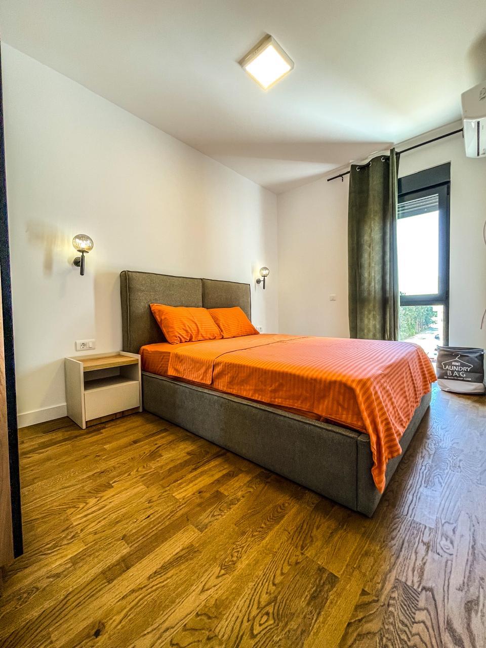 Elegant Ulcinj bedroom with modern gray bed, orange accents, wood floors, natural light&mdash;exclusive at montenegro-listings.me by ekosphere doo.
