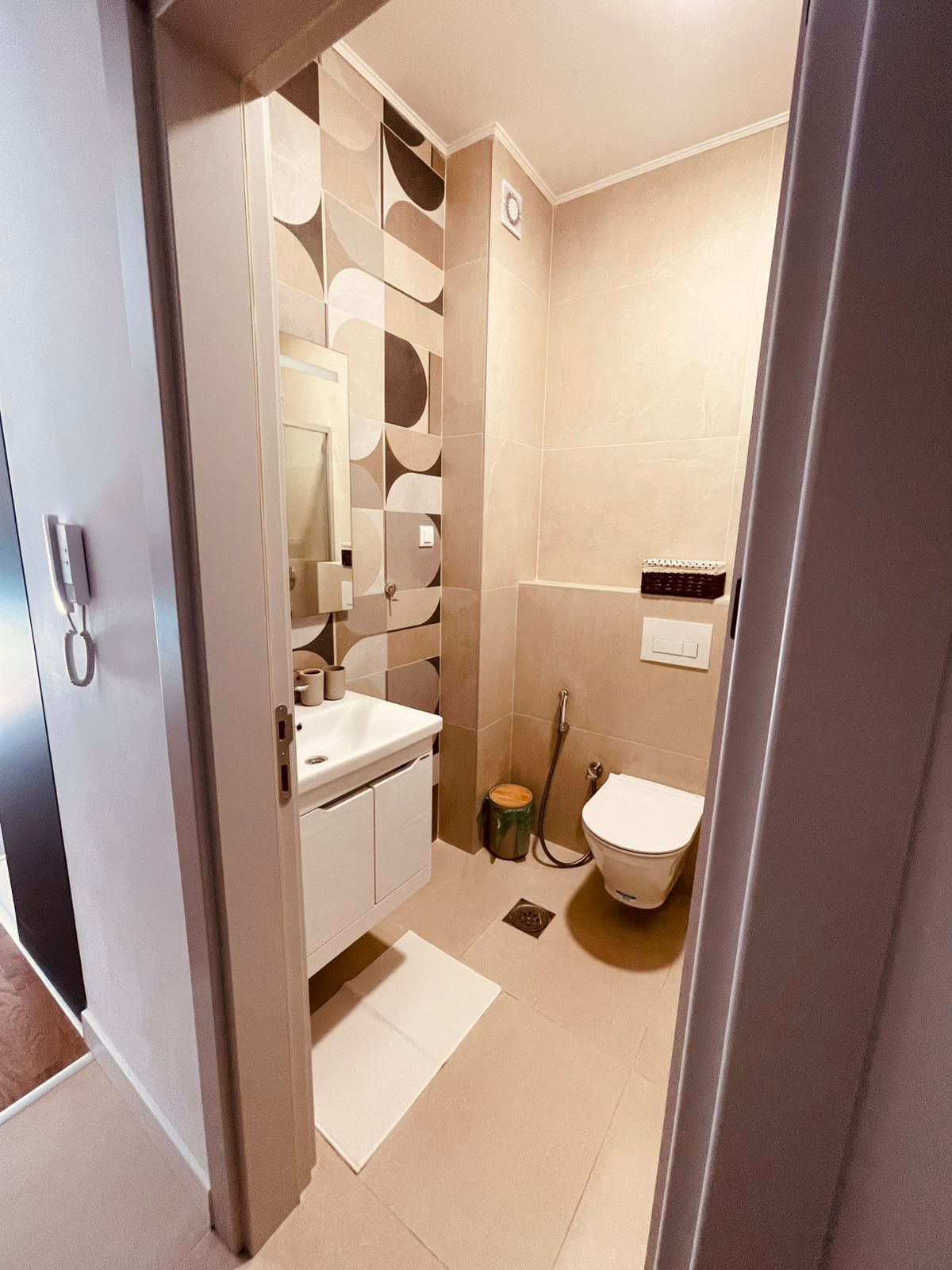 Contemporary bathroom in Ulcinj, Montenegro: beige tiling, wall toilet, stylish sink with mirror—ideal real estate at montenegro-listings.me.