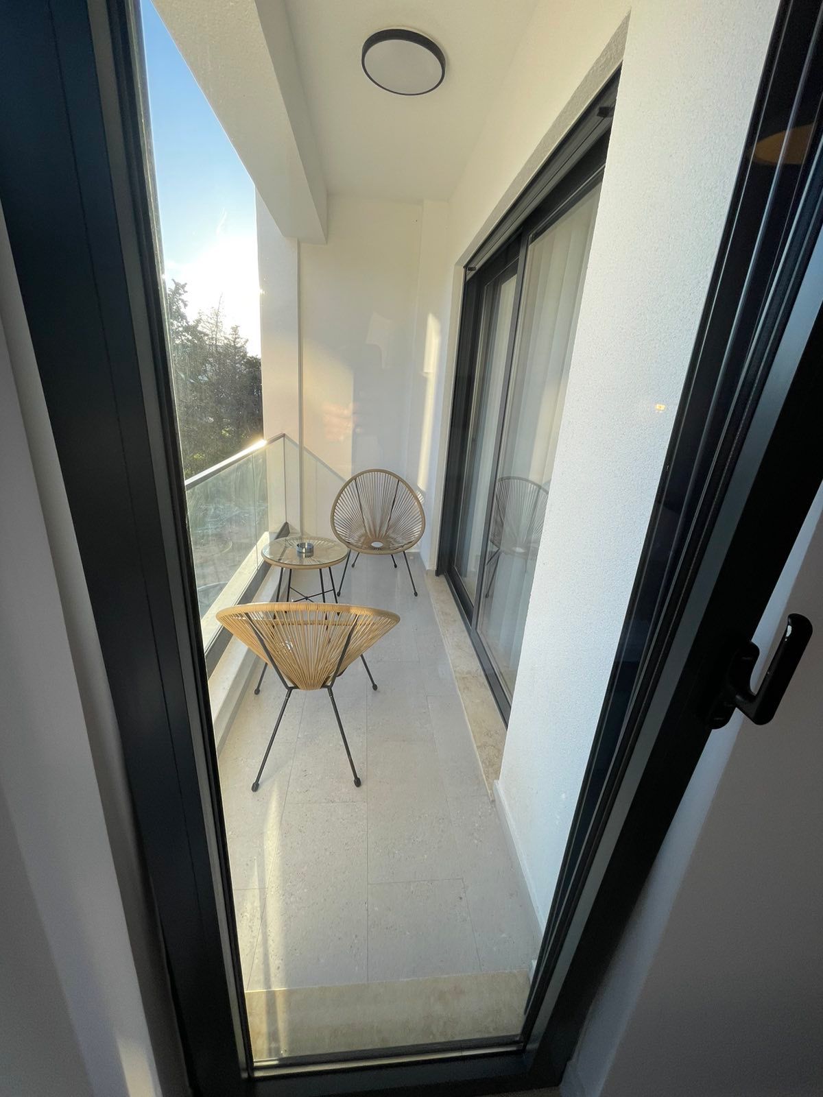 Modern balcony in Ulcinj with wicker seating, glass railing, sunny ambiance & lush views&mdash;ideal Montenegro investment on montenegro-listings.me by ekosphere doo.