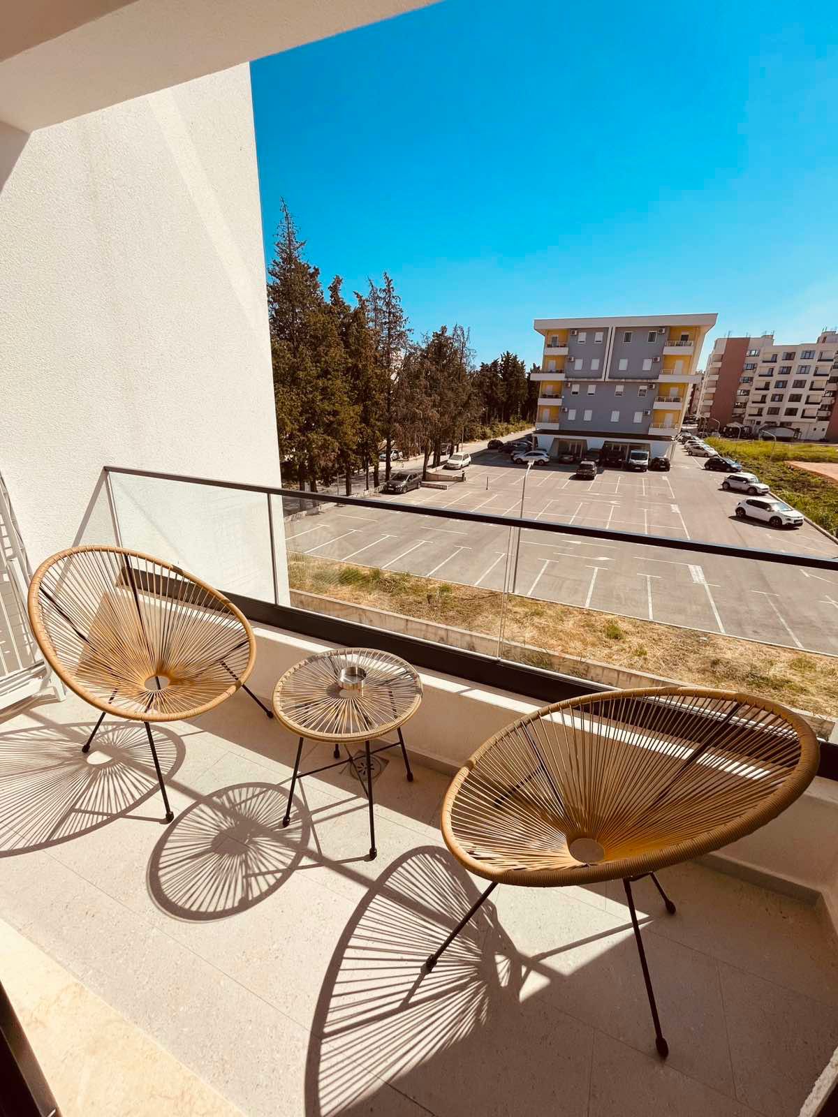 Modern Ulcinj balcony with stylish woven chairs and glass table, scenic view of vibrant complex&mdash;exclusive on montenegro-listings.me.