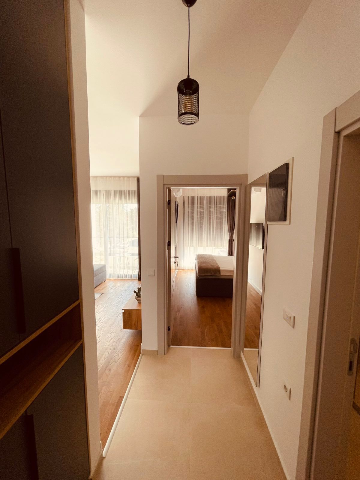 Modern Ulcinj apartment: bright hallway, wooden floors, elegant pendant light, spacious bedroom with large windows. eksophere doo project.