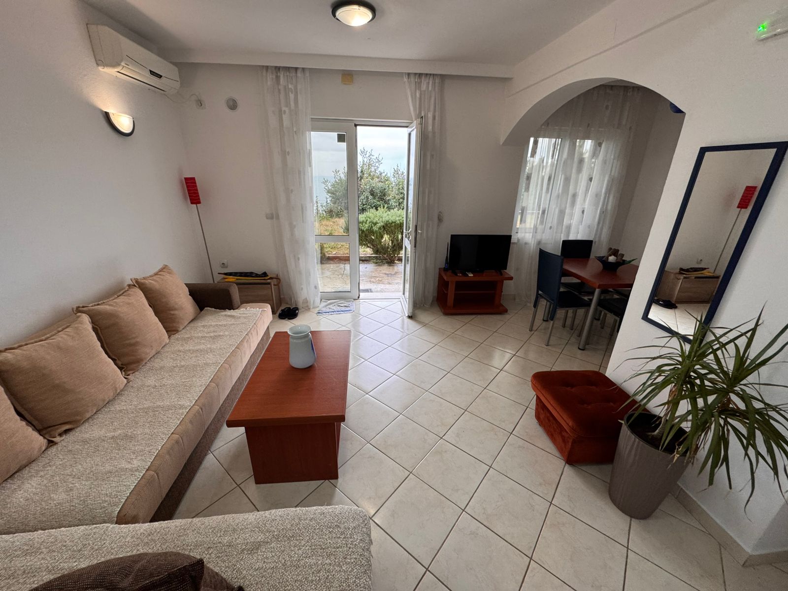 Sonnendurchflutetes Wohnzimmer in Ulcinj mit weißen Fliesen, einem beigen Sofa, Glastüren und moderner Einrichtung – exklusiv auf montenegro-listings.me von ekosphere doo.