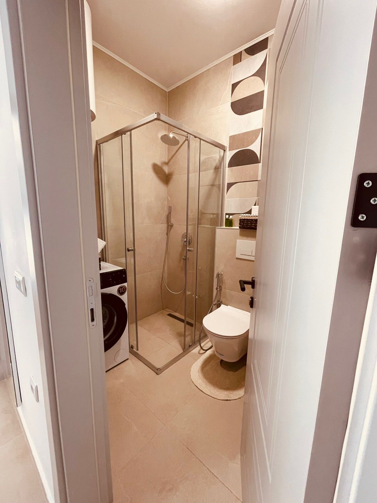 Elegant modern bathroom in Ulcinj with glass shower, wall-toilet, washer, and chic tiles&mdash;ideal Montenegro investment via ekosphere doo.