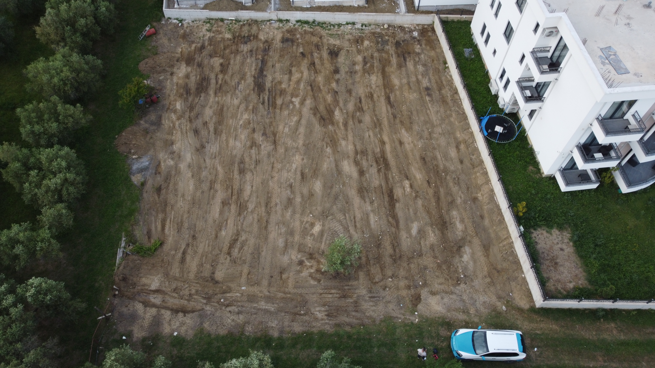 Prime Ulcinj investment: Spacious cleared lot beside modern white apartments, surrounded by lush trees. Exclusive at montenegro-listings.me by ekosphere doo.