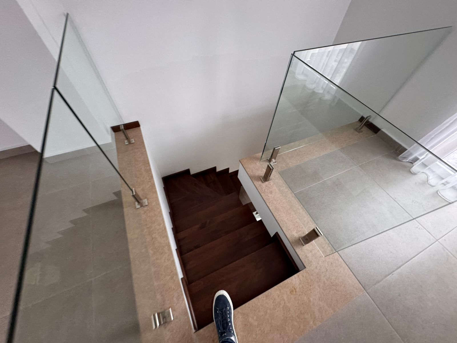 Elegant Ulcinj staircase with glass railings, dark wood steps, and tiled floors. Bright, modern investment via montenegro-listings.me by ekosphere doo.