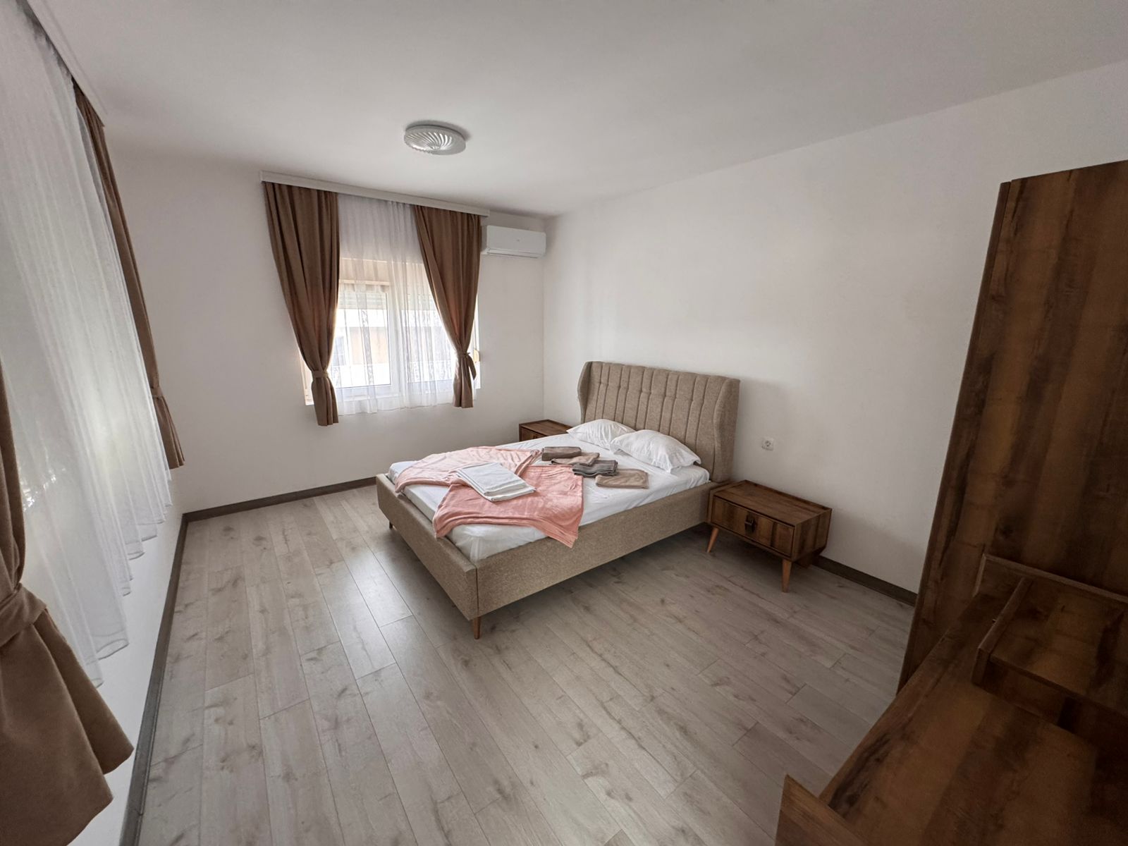 Modern Ulcinj bedroom for sale&mdash;double bed, elegant wood furnishings, bright window with brown curtains. Invest at montenegro-listings.me by ekosphere doo.