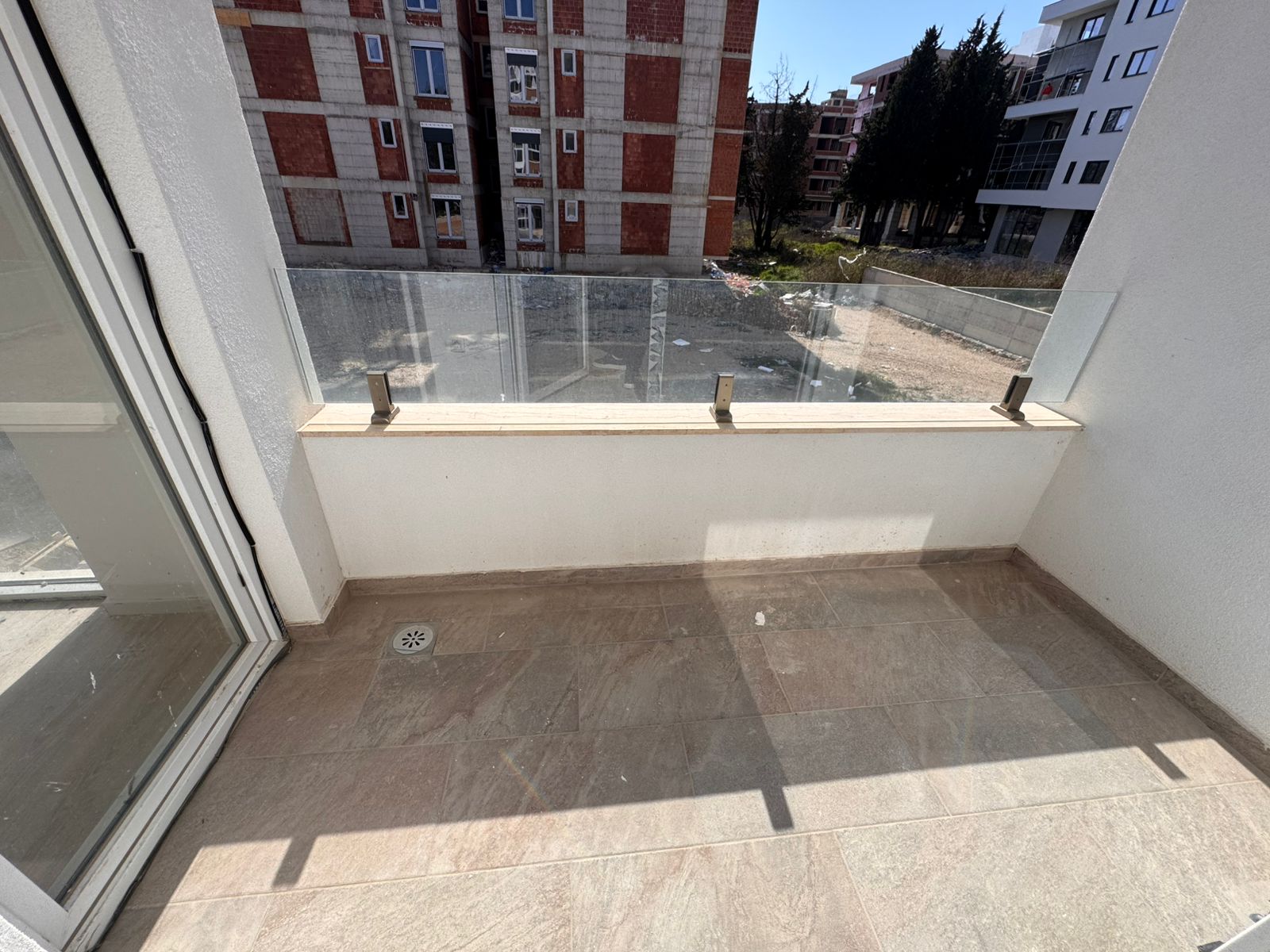 Modern tiled balcony with glass railing, sunlit views over Ulcinj&rsquo;s growing property market. Exclusive at montenegro-listings.me by ekosphere doo.